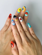 Hand model wearing short handmade nails with retro color palette, smiley emojis, peace signs, and daisy accents